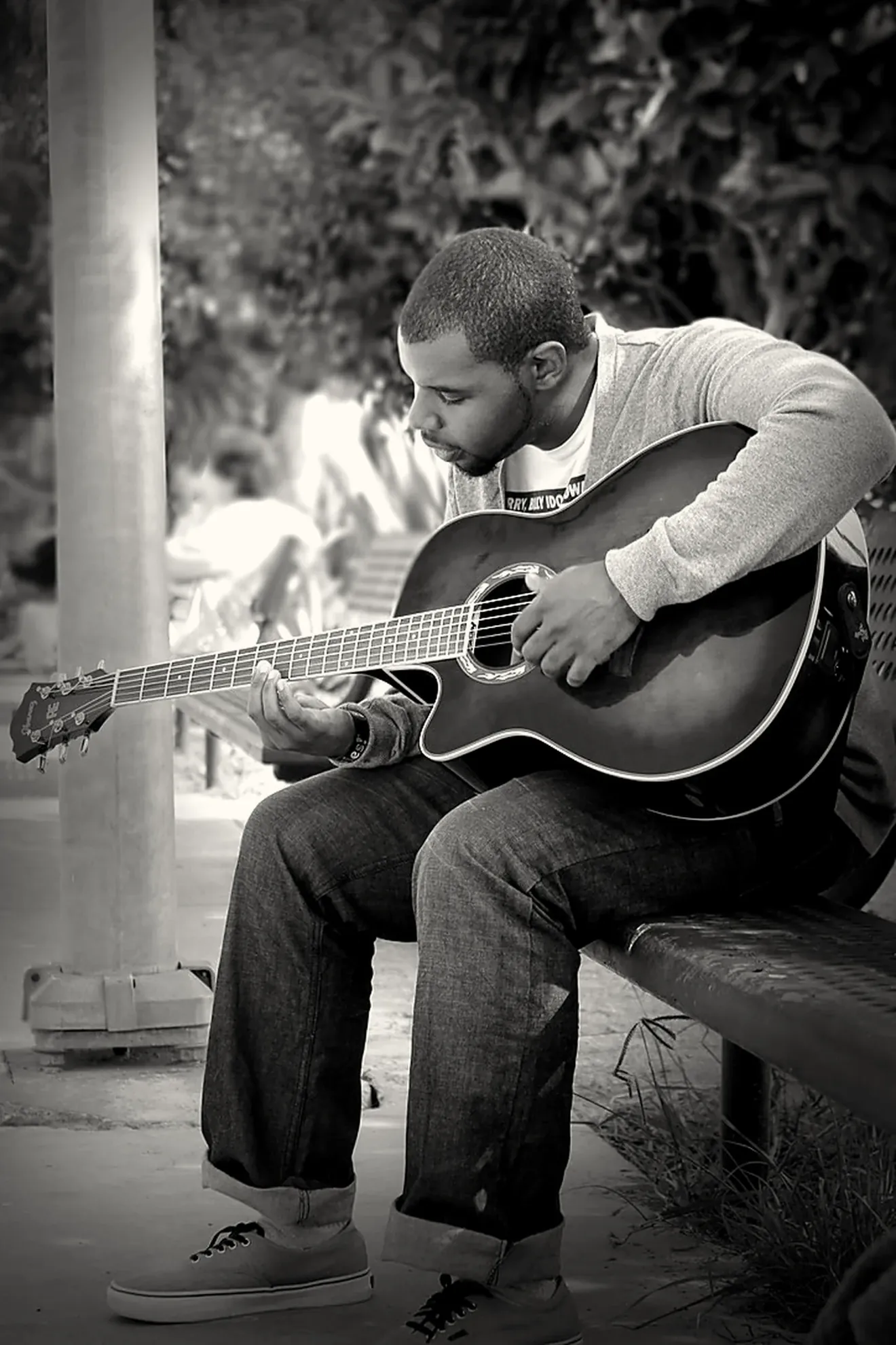 Matthew Scott playing an acoustic guitar on a park bench